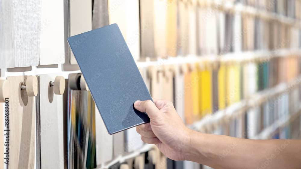 Wall mural designer hand picking samples board from material swatch wall display in material library. choosing 