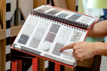 Designer hand pointing at sample stone material texture on furniture finishing catalog in material...