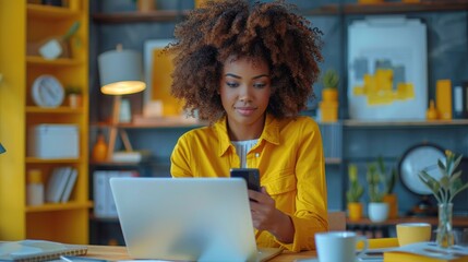 Fototapeta premium Woman in yellow shirt working on a laptop and using a smartphone at a cozy home office with colorful decor.