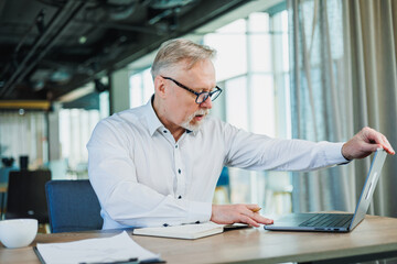 Adult gray haired man businessman lawyer clothes classic formal shirt work in office hold documents document accounting folder. A gray-haired man works in the office with a laptop