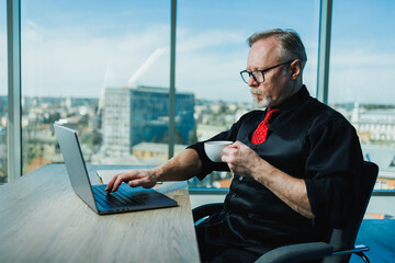 Male gray-haired stylish freelancer working with laptop, gray-haired businessman at workplace in...