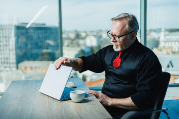 Male gray-haired stylish freelancer working with laptop, gray-haired businessman at workplace in...