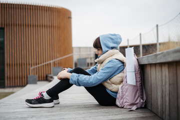 Sad girl alone, sitting in front of school building, waiting for parents. Young schoolgirl with no...