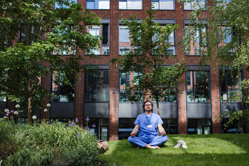 Doctor sitting on grass, meditating and relaxing, winding down from busy workday in hospital....