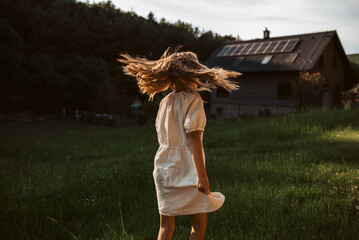 Little girl in front of house with solar panels on roof, jumping, dancing and having fun. Concept...