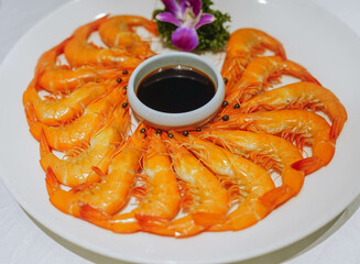 Boiled shrimps on white dish with soy sauce in small bowl in centre