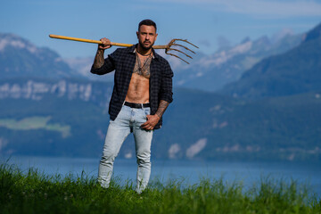 European Farmer with muscular torso on hay field in countryside. Rural Swiss, rural Alps. Male...