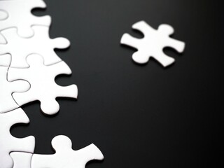 Obraz premium Unfinished white jigsaw puzzle on a black background and copy space