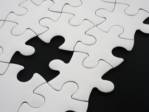 Incomplete white jigsaw puzzle with one missing piece on a black background
