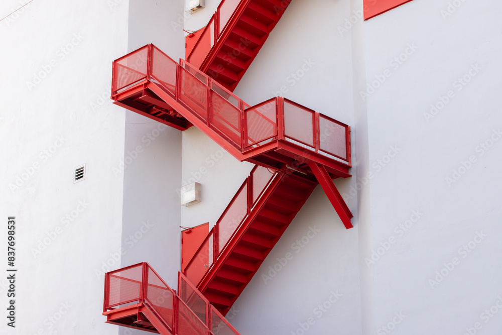 Wall mural a red staircase with a white building in the background. fire escape ladder outside of building.