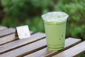 A green matcha tea drink in a plastic cup sits on a wooden table with garden background.