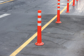 A row of orange and white traffic cones are lined up on a street. orange plastic bollards on...