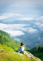 Naklejka premium Woman sits in nature above the clouds and enjoy nature panorama. Georgia travel pristine nature