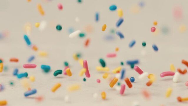 Rainbow sprinkles falling and bouncing on white back drop in slow motion birthday party celebrate