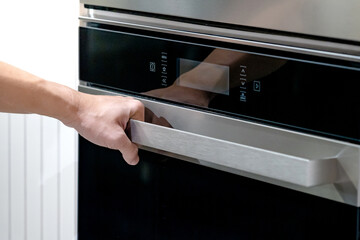 Male hand holding handle bar opening electric oven door in kitchen showroom. Shopping cooking appliance for domestic kitchen