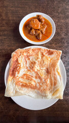 Top view picture of "roti canai telur" with lamb curry on table during breakfast. A flatbread mix with egg.