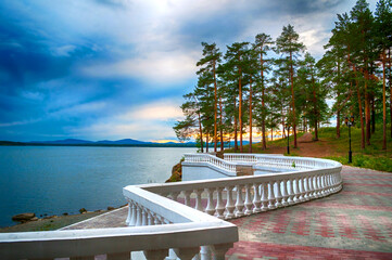Summer cloudy scene- summer trees at the edge of the cliff and lake under dramatic stormy sky
