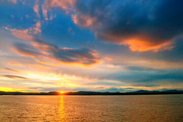 Sea landscape - sea waters lit by sunset summer light. Sea summer nature with mountain range and colorful clouds