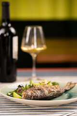 Grilled fish and white wine in the background. Restaurant dinner concept