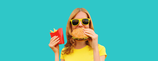 Portrait of happy cheerful young woman eating burger fast food and french fries, fried potatoes