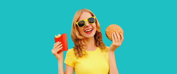 Portrait of happy cheerful young woman eating burger fast food and french fries, fried potatoes