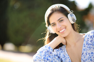 Happy woman wearing headphone looks at camera in a park