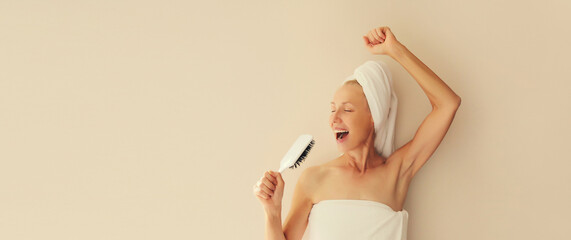 Happy cheerful woman having fun sings with hair comb after shower drying her wet hair with towel