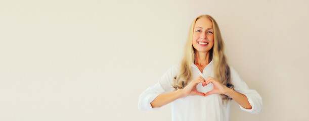 Portrait of happy smiling caucasian woman showing heart shaped gesture sign with hands on her chest