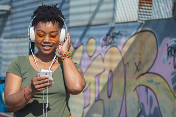 african american urban woman with headphones and phone on graffiti wall
