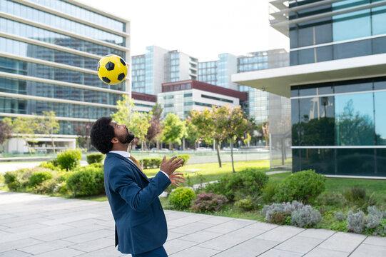Young businessman heading yellow soccer ball in office park