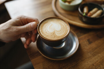 A close-up shot of a man enjoying a fragrant cup of freshly brewed coffee at a cafe during breakfast.
