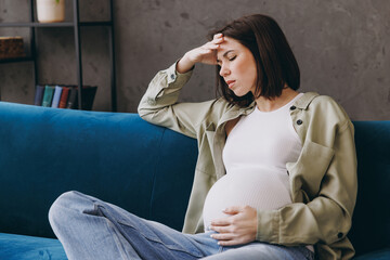 Young upset depressed sad minded tired pregnant woman with belly she wear casual clothes sit on...