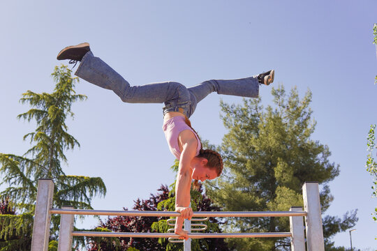 Active woman practicing handstand on parallel bars at park on sunny day