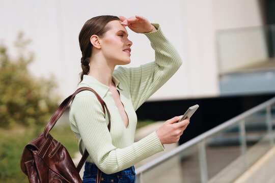 Woman holding smartphone and shielding eyes near railing