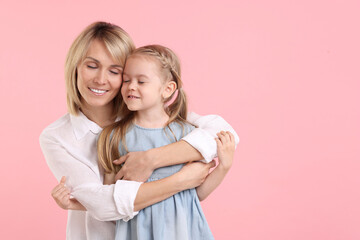 Mother hugging her happy daughter on pink background. Space for text