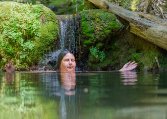 woman submerged in a river cooling off under a crystal clear waterfall