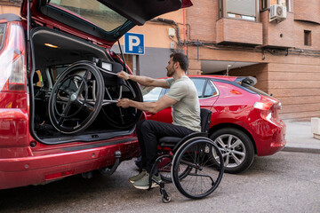 Disabled man in wheelchair loading handcycle in car trunk