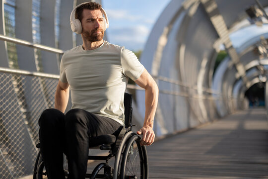 Man with disability enjoying music through wireless headphone and sitting on wheelchair at bridge