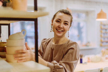 Happy businesswoman arranging handmade clay crockery in workshop
