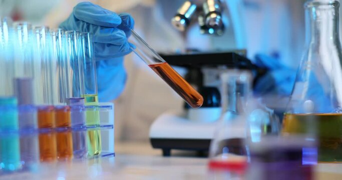 Scientist mixes chemicals in laboratory and holds test tube with orange liquid
