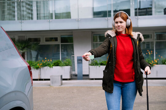 Smiling woman wearing wireless headphones and unlocking car with remote control key
