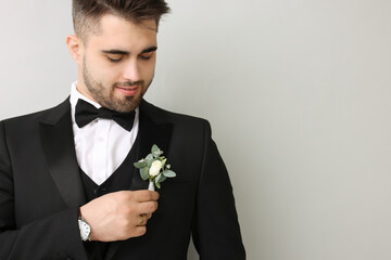 Handsome young groom with boutonniere on light grey background, space for text. Wedding accessory