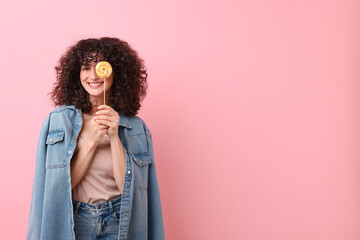 Beautiful woman covering eye with lollipop on pink background, space for text