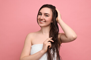 Fototapeta premium Young woman applying hair mask on pink background