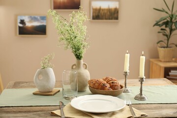 Clean tableware, candlesticks, flowers and fresh pastries on table in stylish dining room