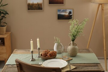 Clean tableware, candlesticks, flowers and fresh pastries on table in stylish dining room