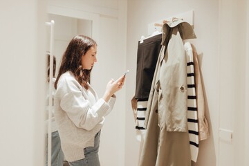 Korean teenage girl takes a selfie in new clothes in the mirror and sends it to her friend via phone in a shopping mall. Retail and consumerism. Sale promotion and shopping concept. Part of a series