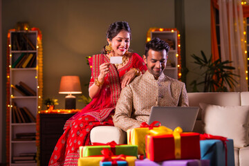 Indian asian young couple celebrating diwali and online shopping on laptop at home
