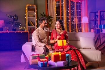 Indian young couple posing with gift boxes on diwali festival evening at home