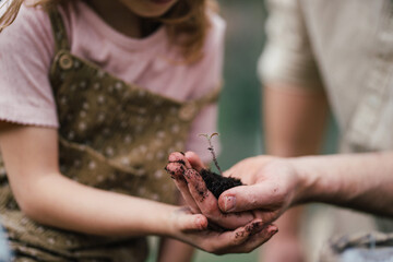 Fater and girl with seedling in palm, working together in garden, planting seedlings, spending time togeter, have shared hobby. Fatherhood and Father's Day concept.